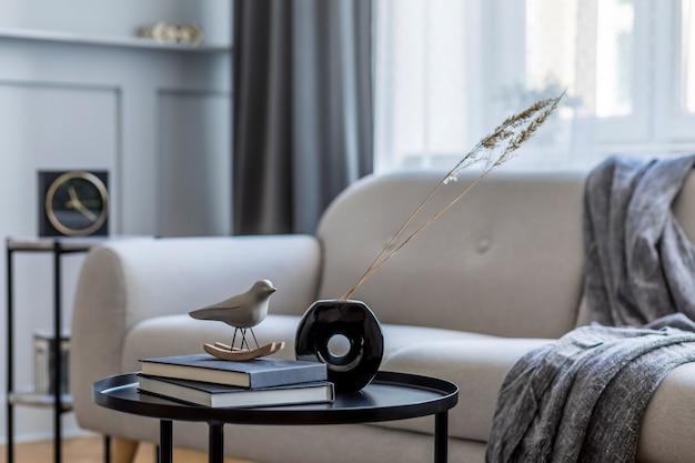 Diseño de interiores de sala de estar con elegante sofá gris, cuadros, mesa de café, taburete, libros, flores secas y elegantes accesorios en la decoración del hogar moderno.
