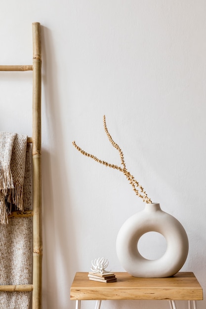 Diseño de interiores de sala de estar con elegantes flores secas en jarrón, escalera de madera, cuadros y accesorios personales en la decoración del hogar moderno.