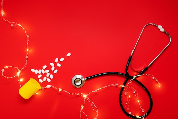 Diseño médico sobre un fondo rojo con una hermosa guirnalda de un estetoscopio un árbol de Navidad hecho de pastillas. concepto de feliz navidad para médicos y clínicas médicas.