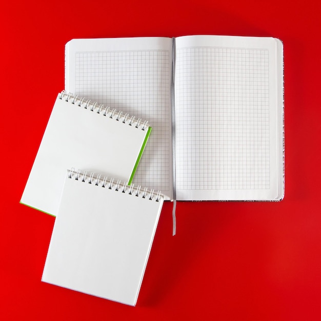 Diseño minimalista para el diseño. Suministros de oficina: cuadernos y bolígrafos sobre un fondo rojo. Abra el cuaderno en blanco para sus notas sobre un fondo rojo.