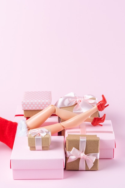 Diseño navideño creativo hecho con patas de muñeca y cajas de regalo en rosa.