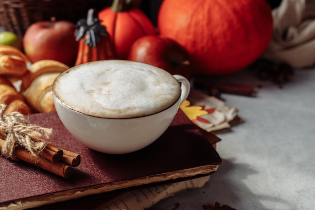 Diseño de otoño. una taza de café, una calabaza, manzanas y especias yacen cerca del libro