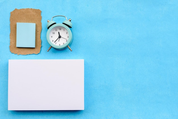 Foto diseño de papelería sobre un fondo azul, una pila de tarjetas blancas, un despertador y un trozo de papel kraft roto