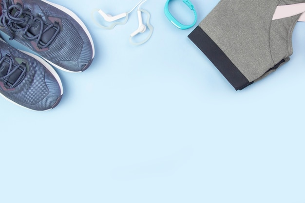 Diseño plano deportivo. Accesorios de fitness zapatillas, ropa, auriculares y relojes sobre un fondo azul. Hacer deporte y fitness en casa.