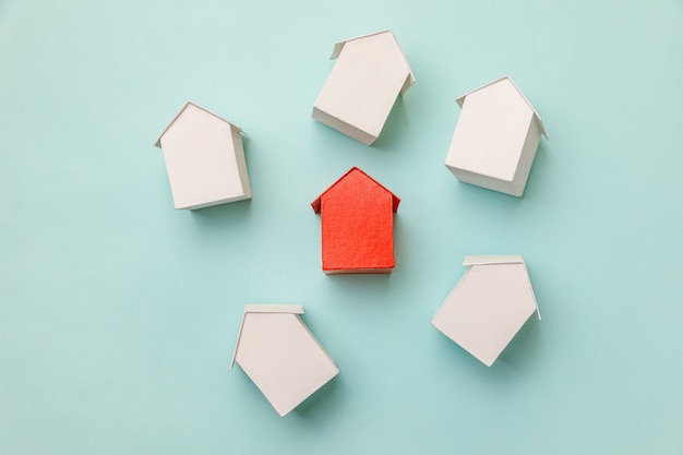 Foto diseño plano simplemente con casa modelo de juguete rojo en miniatura entre casas blancas aisladas en b ...