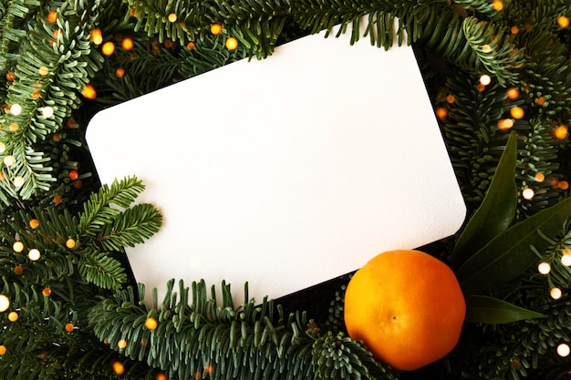 Diseño de ramas de árboles de navidad con tarjeta de papel blanco y mandarina fresca