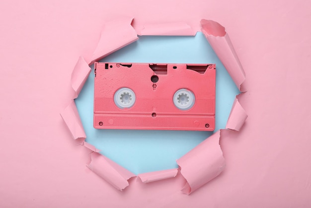 Diseño retro creativo Cassette de video rosa a través del agujero rasgado de papel rosa Minimalismo Arte conceptual Lay plano Vista superior