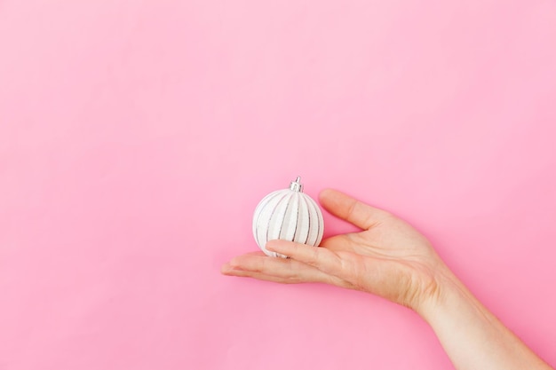 Diseño simple minimalista mano femenina mujer sosteniendo bola de adorno de navidad aislado en color rosa pastel ...