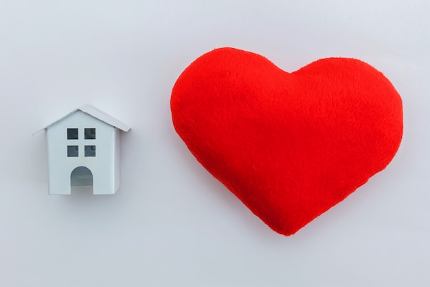 Diseño simplemente minimalista con casa de juguete blanca en miniatura con corazón rojo aislado en blanco