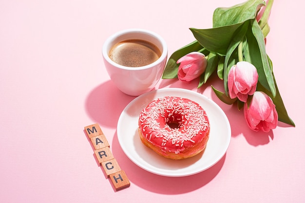 Diseño de tarjeta de felicitación del 8 de marzo con una taza de café y un platillo con una rosquilla formando el número ocho y un tierno tulipán rosa cerca