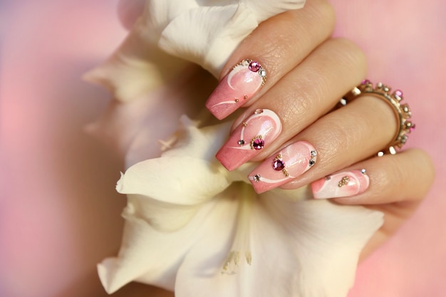 Diseño de uñas rosa claro con líneas blancas, pedrería, purpurina con gladiolos.