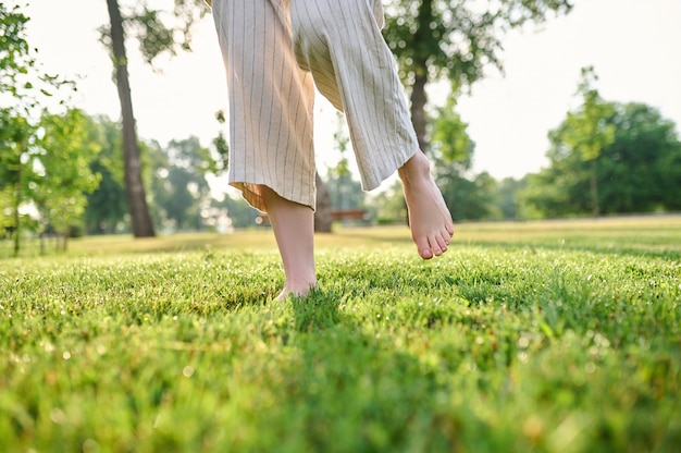 Disfruta cada momento. Pies descalzos femeninos moviéndose con alegría sobre la hierba verde en el parque en un día soleado, sin rostro