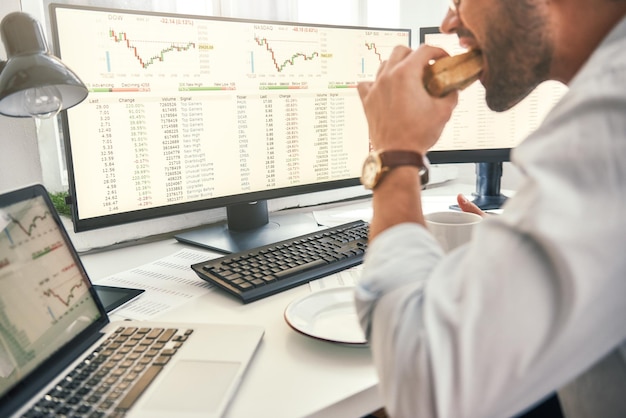 Disfrutando del almuerzo, el primer plano del comerciante barbudo está comiendo un sándwich fresco y mirando la pantalla del monitor