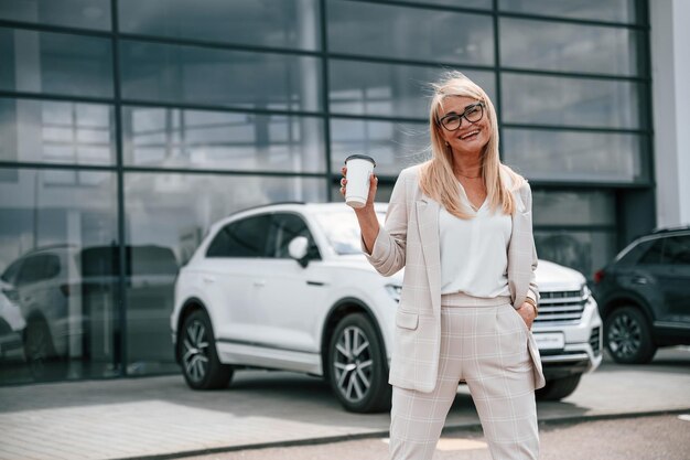 Disfrutando de una bebida fresca Una mujer con ropa formal blanca está en el concesionario de automóviles