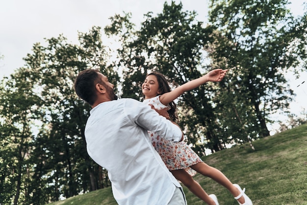 Disfrutando cada minuto juntos. Padre amoroso joven que lleva a su hija sonriente mientras pasa tiempo libre al aire libre