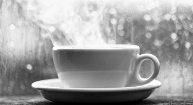 Foto disfrutando del café en un día lluvioso café recién hecho en una taza blanca o taza en el alféizar de la ventana hora del café en un día lluvioso ventana de vidrio mojado y una taza de café caliente el clima nublado de otoño es mejor con bebida de cafeína