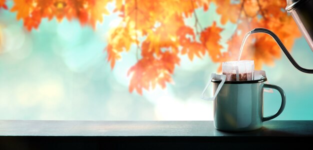 Disfrutando del café en otoño y otoño. Hacer café caliente vertiendo agua de la tetera en una bolsa de goteo de café instantáneo. Árbol de hoja de arce borrosa como fondo