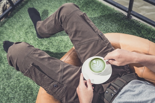 Disfrutando de café recién hecho. Hombre con pantalones cargo y sosteniendo una taza mientras se relaja en el sofá en casa