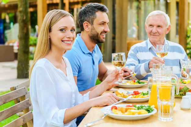 Disfrutando de una cena en familia. Familia feliz disfrutando de la comida juntos mientras mujer sosteniendo una copa de vino y sonriendo