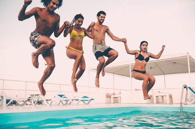 Disfrutando de la fiesta en la piscina. Grupo de gente joven hermosa que parece feliz mientras salta a la piscina juntos