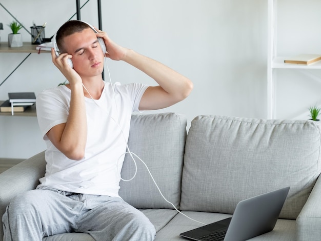 Disfrutando de la música Hombre tranquilo Relajación del sonido Inspirado chico casual escuchando la melodía favorita en los auriculares que se conectan al sofá portátil sentado en el interior de la sala de luz