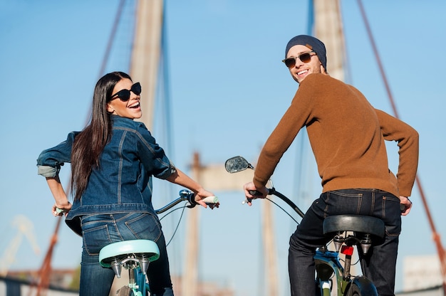 Foto disfrutando de un paseo divertido. vista trasera de la hermosa pareja joven en bicicleta y mirando por encima del hombro con una sonrisa