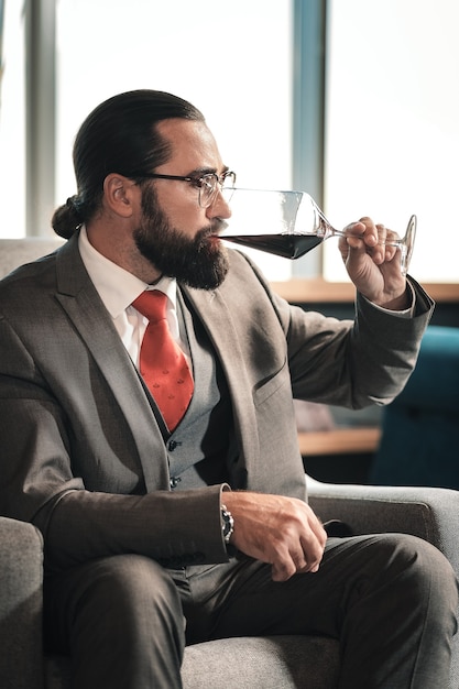 Disfrutando del sabor. Abogado con experiencia, barbudo y moreno que disfruta del sabor del vino tinto después de la jornada laboral