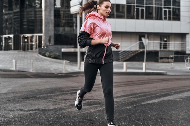 Disfrutando de su carrera. Longitud total de mujer joven atractiva en ropa deportiva corriendo por la calle