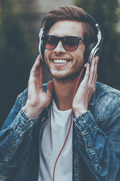 Disfrutando de su música favorita. Joven alegre en auriculares escuchando música y sonriendo