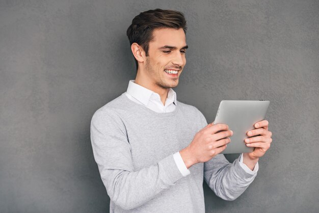 Disfrutando de su tableta digital. Hombre joven confidente que sostiene su tableta digital