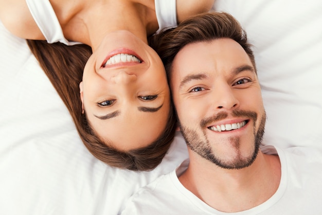 Disfrutando de su tiempo juntos. Vista superior de la hermosa joven pareja amorosa acostada en la cama juntos y sonriendo