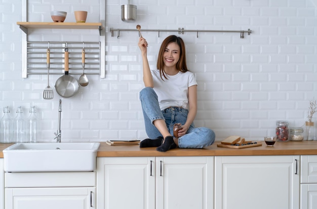 Foto disfrutando del tiempo en casa retrato de una joven asiática bastante exuberante con un estilo informal disfrutando de comer delicioso chocolate de un frasco mientras se sienta en la encimera de la cocina en casa