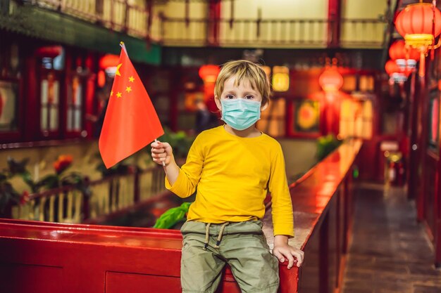 Disfrutando de vacaciones en china niño turista feliz en máscara médica con una bandera china en un chino