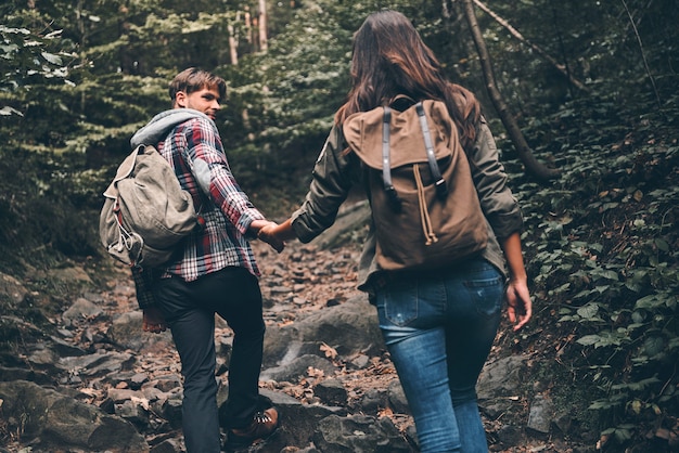 Disfrutando del viaje. Vista trasera de la joven pareja moderna tomados de la mano y subiendo mientras caminaban juntos en el bosque