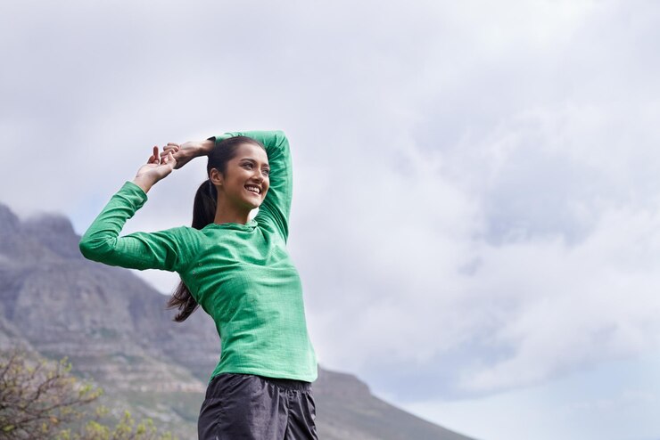 Foto disfrutando de la vista desde la cima una joven mujer étnica estirándose mientras contempla las vistas desde la cima de la montaña