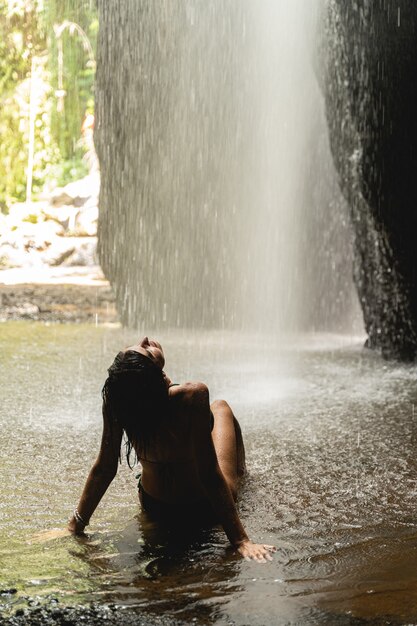 Disfrutar del momento. Amable joven vistiendo traje de baño mientras se detiene cerca de la cascada durante la excursión