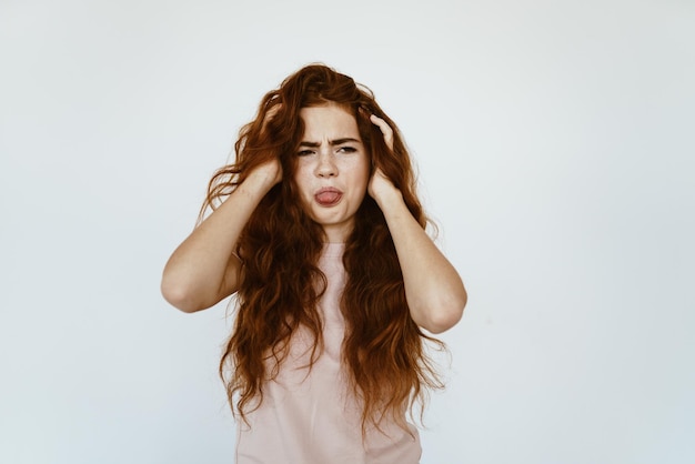 Disgustada sacando la lengua, la chica se frota las manos con su lujoso cabello rojo sobre un fondo gris