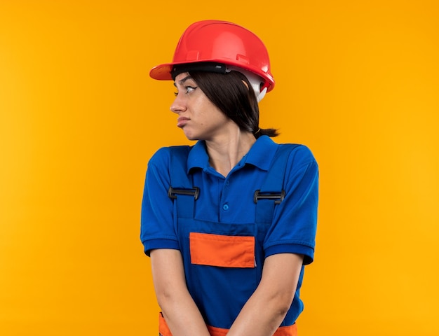Disgustado mirando a la mujer joven constructor de lado en uniforme