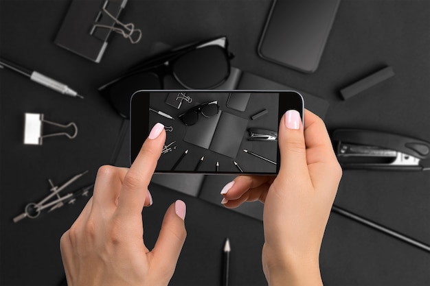 Disparando papelería negra con la cámara del teléfono. Papelería sobre fondo negro. Mano de mujer de primer plano sosteniendo el teléfono.