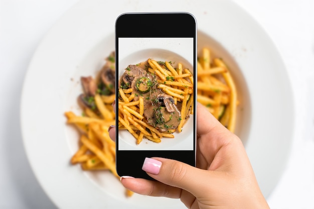 Disparar comida con la cámara del teléfono. Carne con salsa de champiñones y patatas fritas. Fotógrafo de alimentos, plato de disparo de teléfono de mano de primer plano