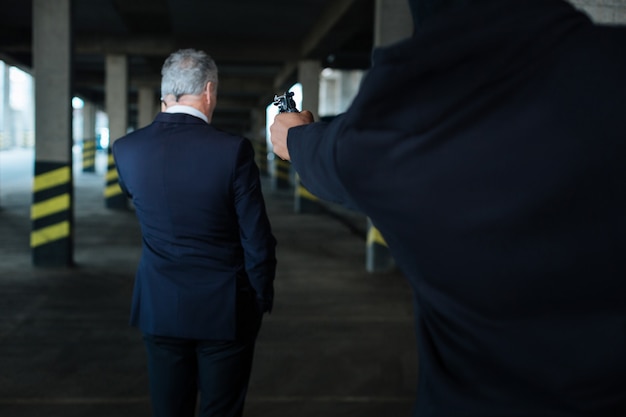 Foto dispararé enojado criminal peligroso fuerte sosteniendo una pistola y apuntando al empresario mientras lo amenaza