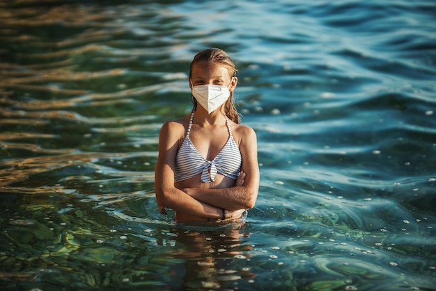 Disparo de un adolescente feliz con mascarilla quirúrgica disfrutando de unas vacaciones en la playa durante el COVID-19. Mirando a la cámara.