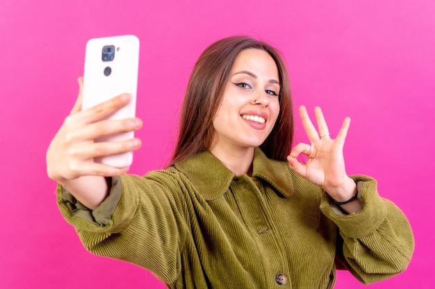 Disparo aislado de una mujer caucásica usando una cámara de teléfono tomando un selfie haciendo el gesto de ok