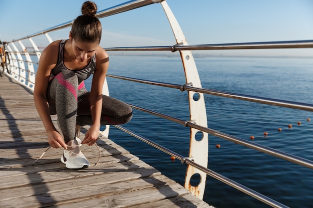 Disparo al aire libre de la atractiva deportista atar los cordones de los zapatos en un muelle