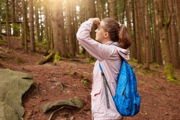 Disparo al aire libre del entusiasta explorador tocando su frente con la mano, cubriéndose los ojos de los rayos del sol, mirando hacia adelante