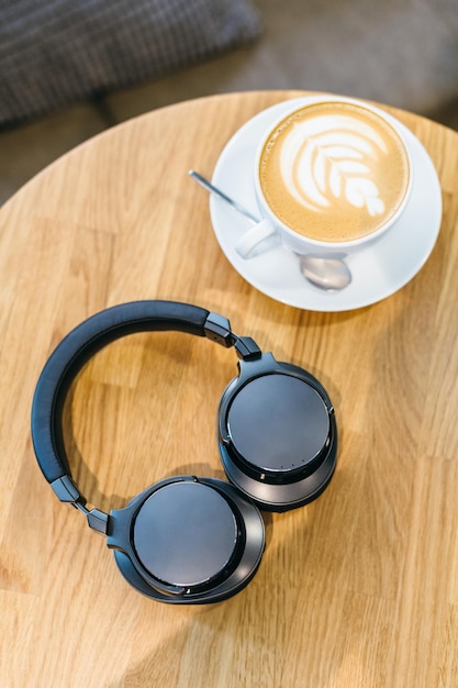 Disparo de auriculares inalámbricos negros y taza de café blanca en la mesa de madera