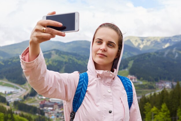 Disparo de bastante joven turista hace selfie en montaña, mujer viajera fotografiada al aire libre contra el hermoso paisaje.