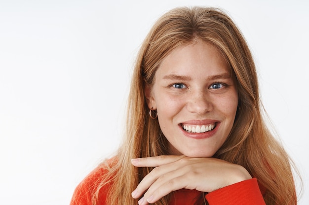 Disparo en la cabeza de una mujer caucásica atractiva carismática feliz con cabello rubio, pecas y ojos azules profundos mirando al frente interesado y alegre con la cabeza apoyada en la palma como si escuchara, sonriendo ampliamente