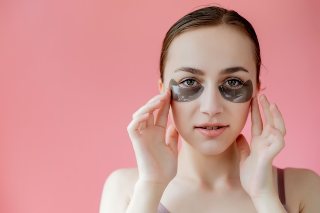 Disparo a la cabeza retrato de cerca sonriente joven con máscara de parches humectantes debajo de los ojos mirando