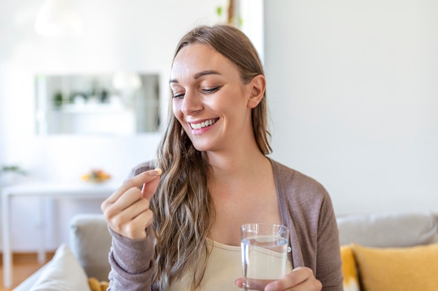 Disparo en la cabeza retrato mujer feliz sostiene píldora vaso de agua toma medicina diaria vitamina D omega 3 suplementos piel pelo uñas fortalecer y belleza medicación para el concepto de cuidado de la salud